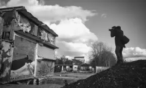Ein Fotograf steht auf einem Hügel und fotografiert ein teilweise zerstörtes, mit Graffiti beschmiertes Gebäude in einer trostlosen Gegend.