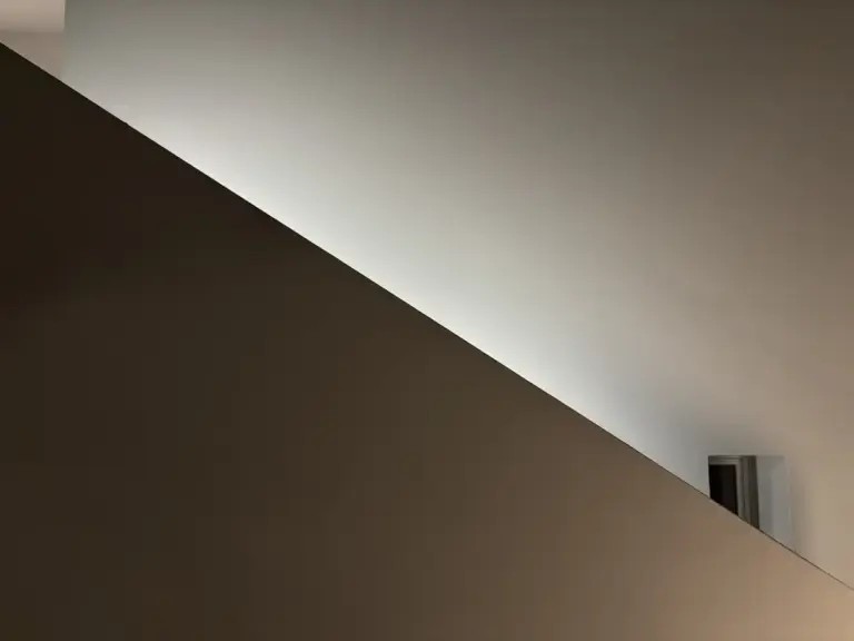 Eine minimalistische Wand mit diagonalem Schatten und einem kleinen rechteckigen Objekt in der rechten unteren Ecke.